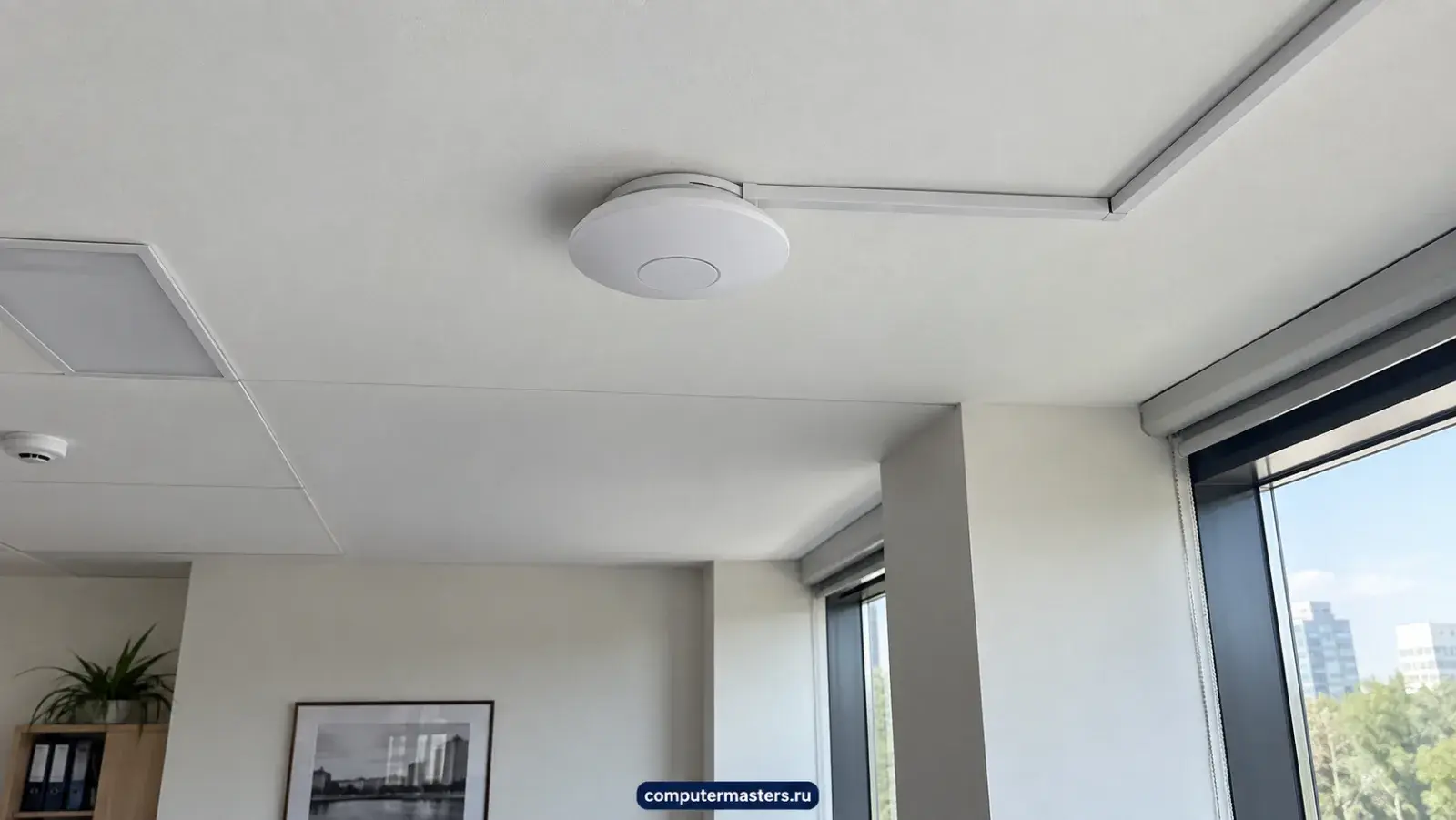 Круглая точка доступа Wi-Fi на потолке офиса, к ней подходит белый кабель-канал