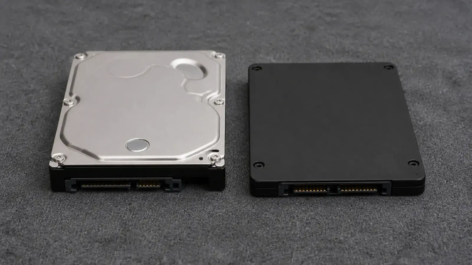 Жёсткий диск 2,5 дюйма и более тонкий SSD лежат рядом на сером коврике разъёмами к камере