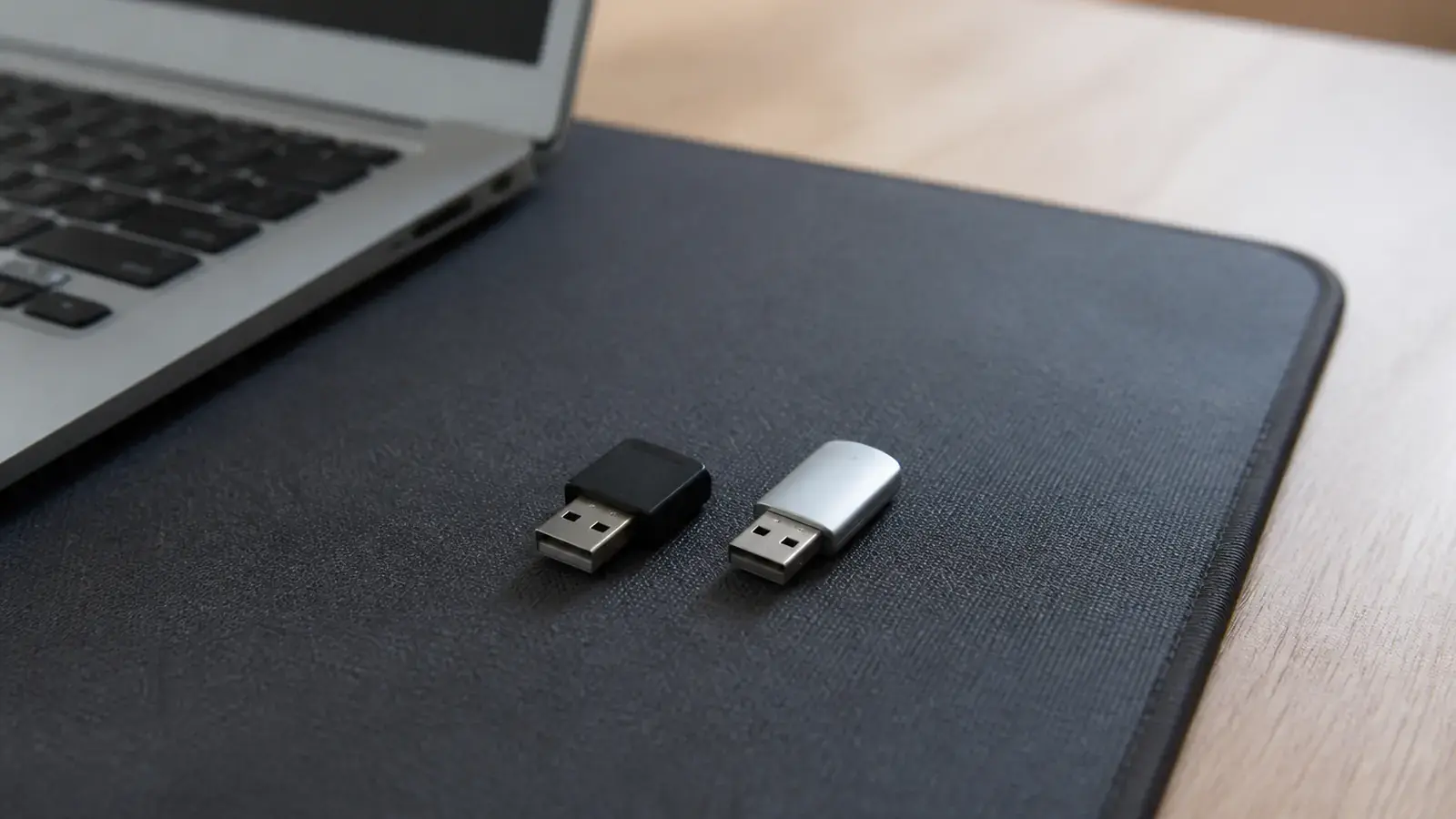 Два небольших USB-токена разной формы, один чёрный и один светло-серый, лежат рядом на коврике для мыши около ноутбука
