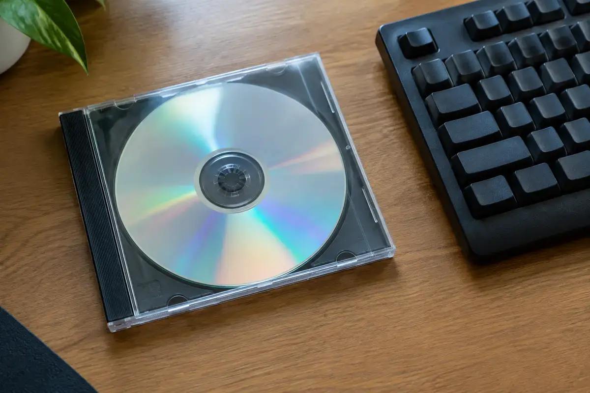 Старый игровой DVD-диск в прозрачной коробке без надписей лежит на деревянном столе рядом с чёрной клавиатурой