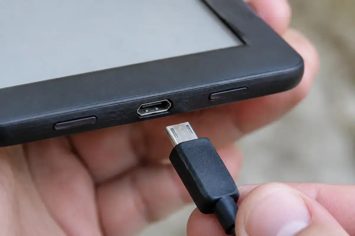 Рука держит читалку, у нижнего торца виден разъём micro-USB, рядом черный штекер перед подключением