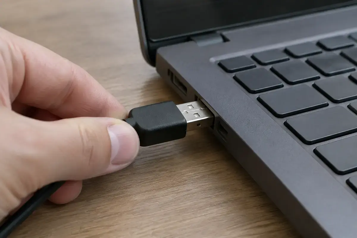 Рука вставляет чёрный USB-штекер в порт на боковой грани тёмно-серого ноутбука